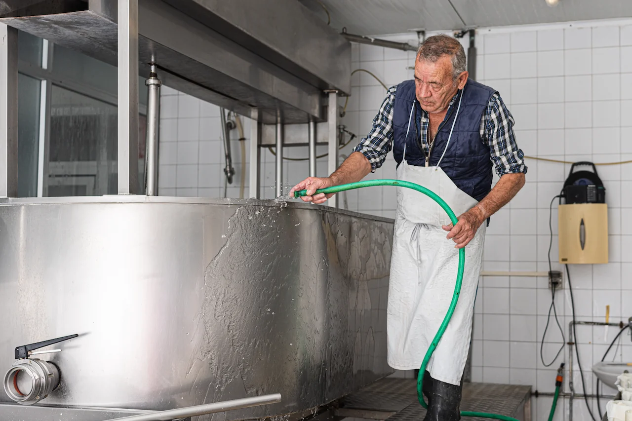 Food manufacturing worker cleaning a large stainless tub